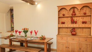 A dining area with a wooden table set for four, flanked by a wooden cabinet with pottery and glassware. - Chequers Barn (Corsham)