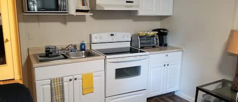 A compact kitchen with white cabinets, a microwave, a toaster, and a stove.