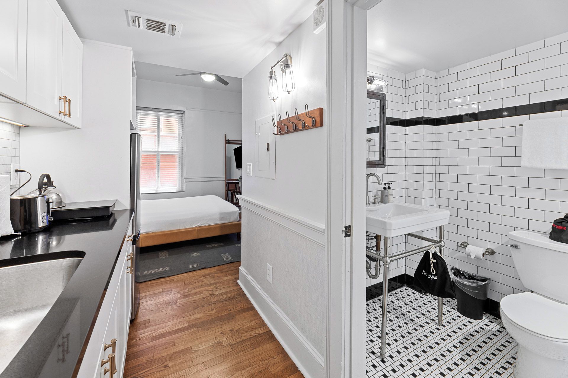 Habitación de hotel pequeña con kitchenette, una cama, un baño con azulejos blancos tipo metro y piso de madera.