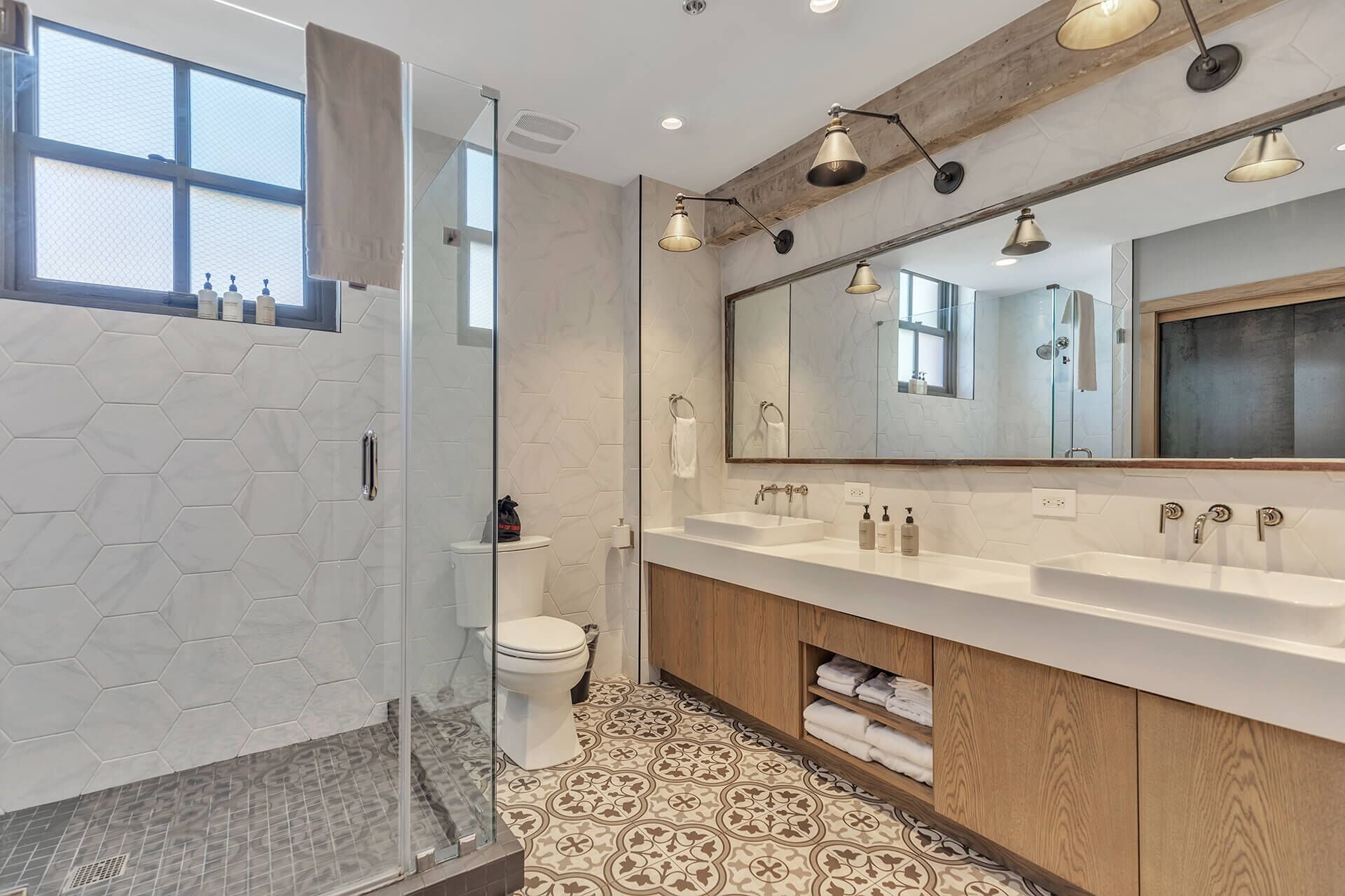 A modern bathroom with a glass shower enclosure, a large mirror, and a wooden vanity.
