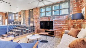 A modern living room with a brick wall, a flat-screen TV, a staircase, and a cozy seating area.