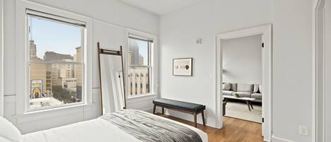 A bedroom with a large bed, a ceiling fan, and a view of the city through the windows.