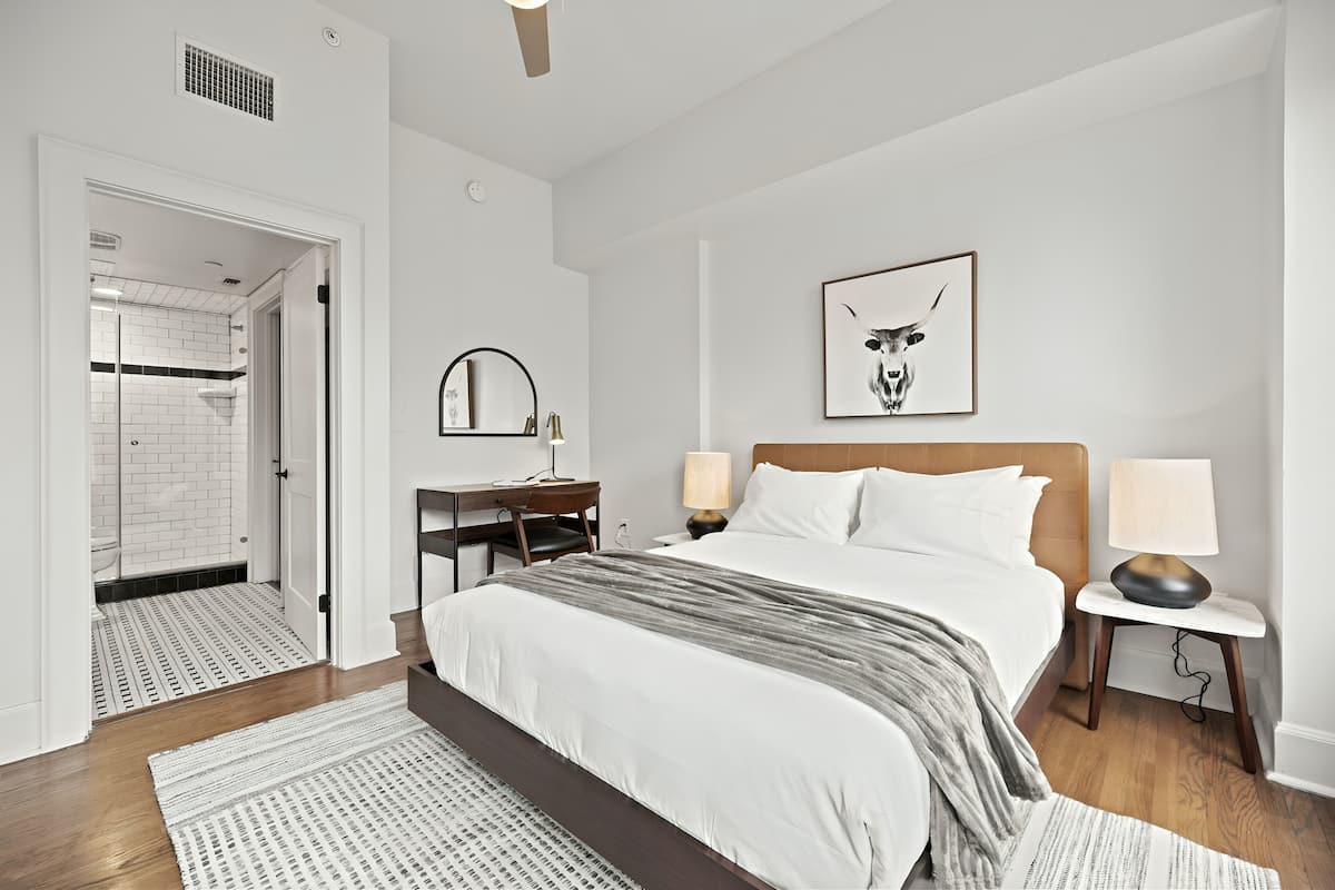 Una habitación de hotel moderna con una cama grande, un escritorio, una mesita de noche y un cuadro en la pared.