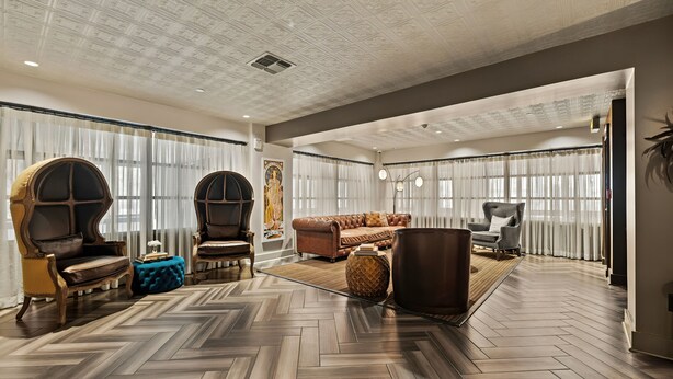 A spacious living area with a herringbone wood floor, large windows with sheer curtains, and a mix of classic and modern furniture.