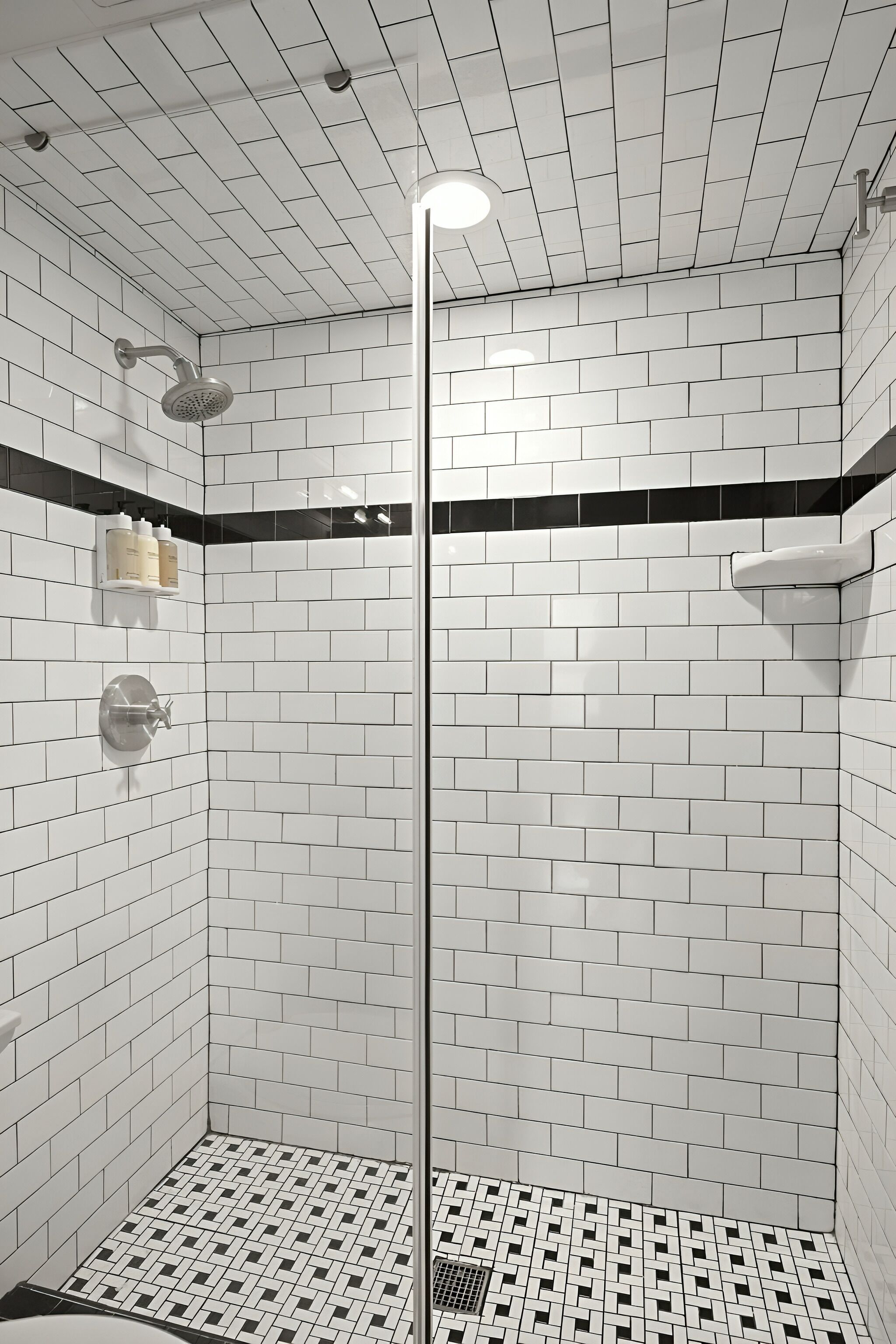 A shower with white and black tiles, a glass door, and a ceiling with recessed lighting.