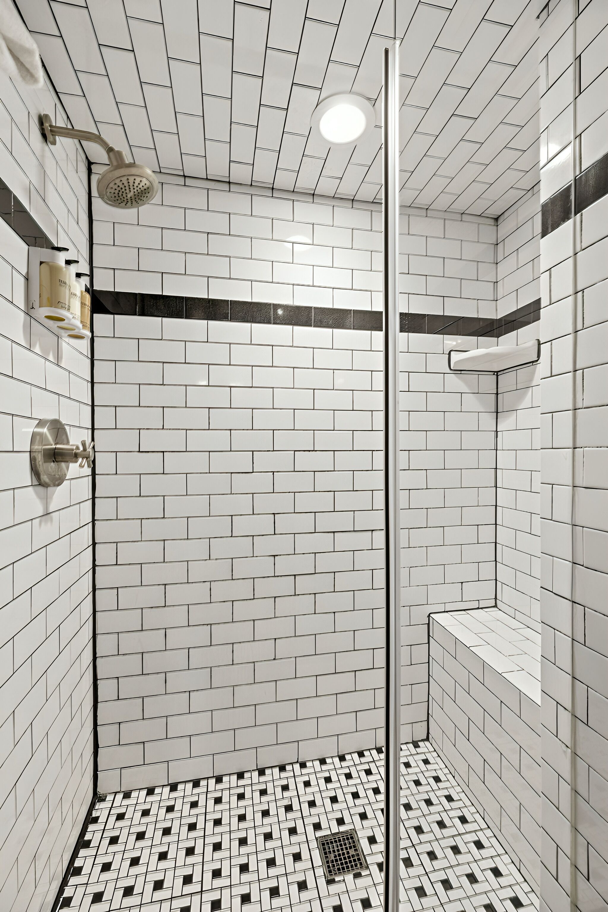 Une douche moderne avec des carreaux blancs et noirs formant un motif, une porte en verre et un éclairage au plafond.