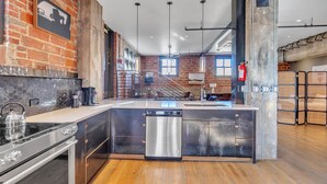 A modern kitchen with a central island, stainless steel appliances, and a brick wall.