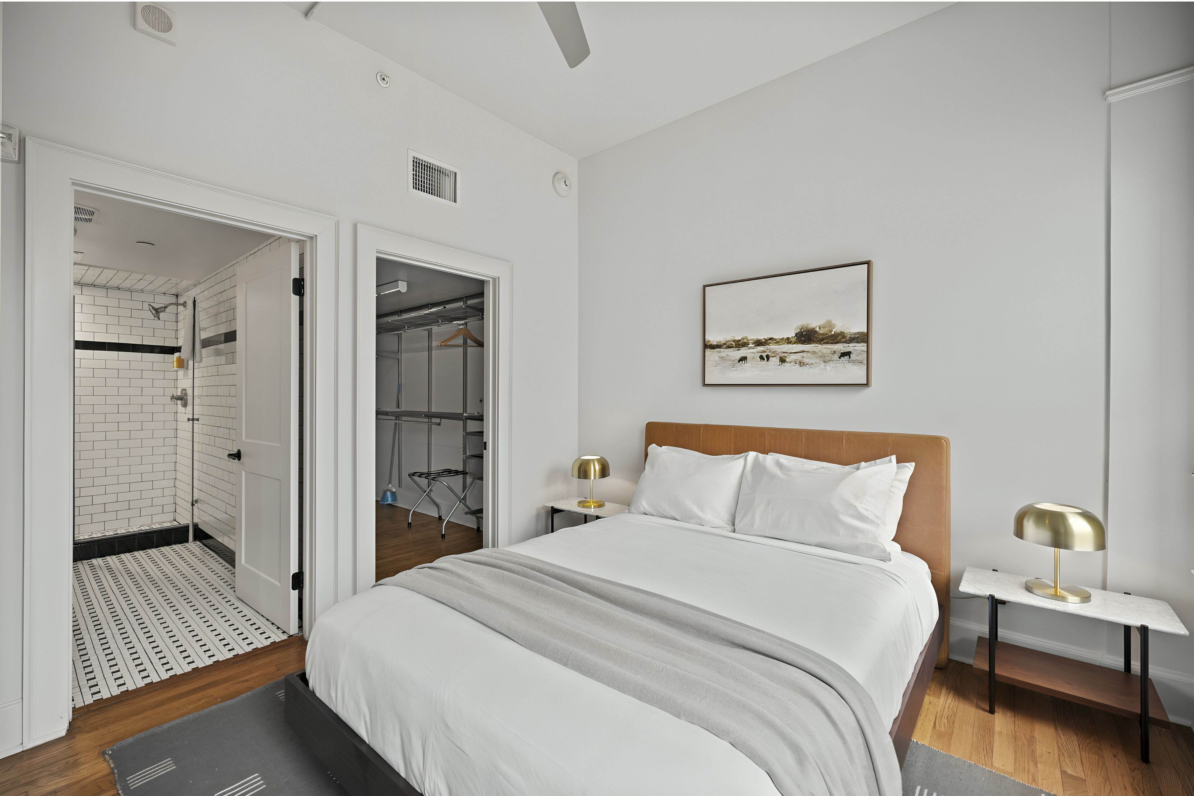 Une chambre moderne avec un grand lit, une tête de lit en bois, un tableau encadré au mur et un dressing.