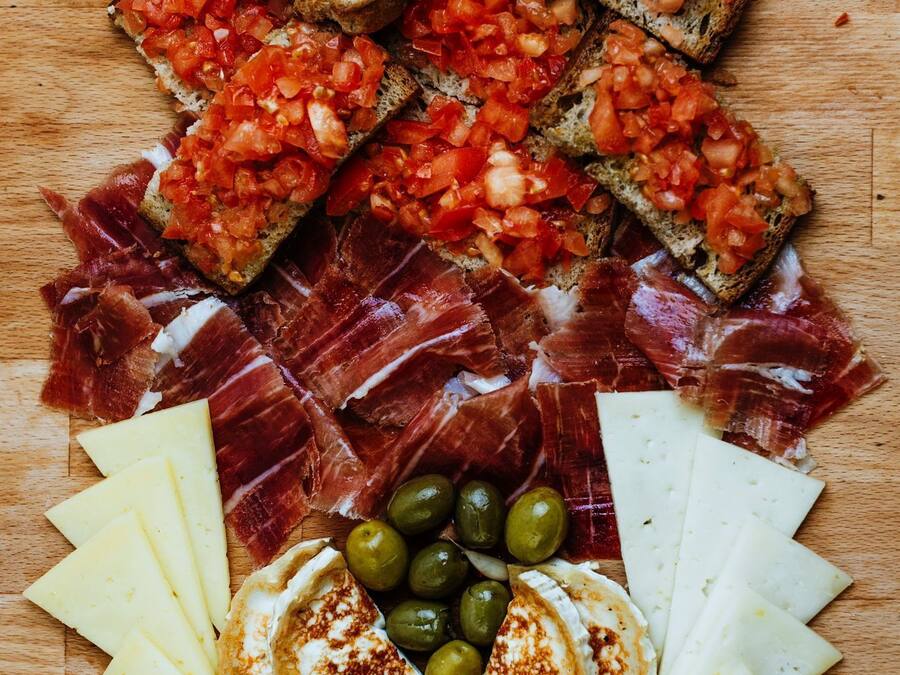 Una tabla de madera con diversos alimentos, incluyendo pan, queso, aceitunas y embutidos.