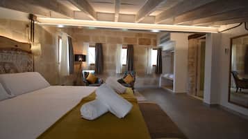 Una habitación de hotel moderna con una cama grande, un espacio de descanso con sofá y sillones, un baño con espejo y una pared de piedra.