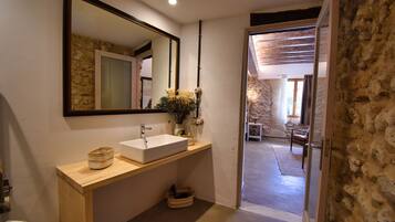 Un baño con tocador de madera, un espejo grande y vistas a una sala de estar con paredes de piedra y techo de madera.
