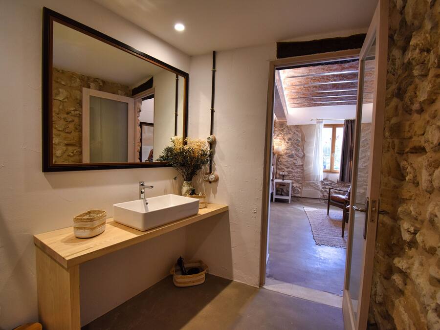 Un baño con tocador de madera, un espejo grande y vistas a una sala de estar con paredes de piedra y techo de madera.