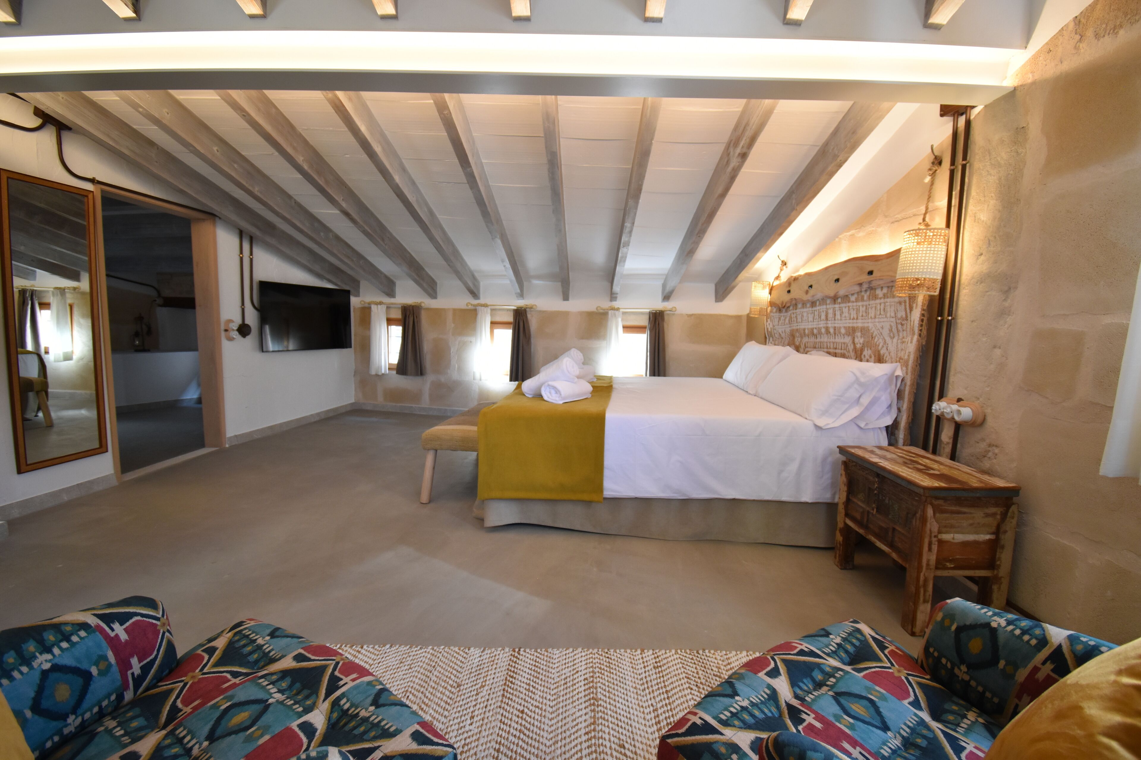 A bedroom with a bed, a wooden bench, a mirror, and a television.