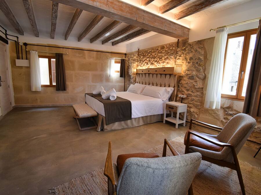 A bedroom with a stone wall, a bed, a bench, a chair, and a small table.
