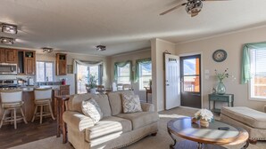 A spacious living room with a beige sofa, a round coffee table, and a kitchen area with wooden cabinets and a microwave.