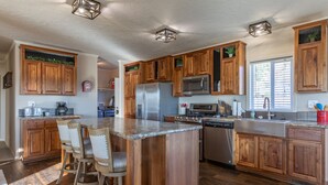 A spacious kitchen with wooden cabinets, a central island with bar stools, stainless steel appliances, and a large window providing natural light.