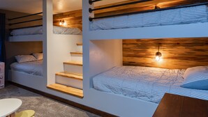 A bunk bed room with wooden beams, a staircase, and a small table.