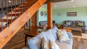 A spacious living area with a wooden staircase, a grey sofa set, and a brown leather couch.