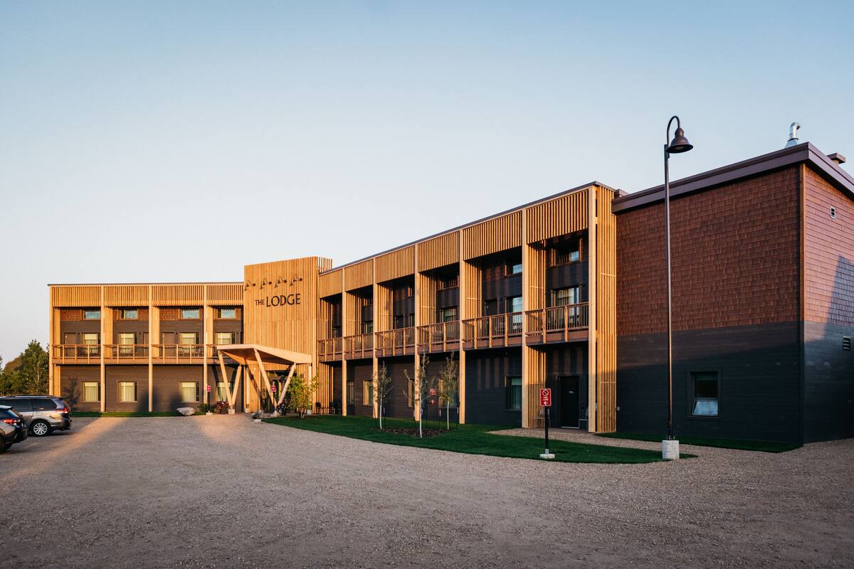 Een modern gebouw met een houten gevel, meerdere balkons en een grindpad.
