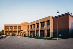 A modern building with a wooden facade, multiple balconies, and a gravel driveway.