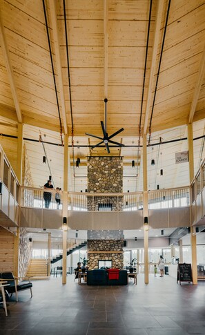 Un intérieur spacieux à plusieurs niveaux, avec des poutres en bois, une grande cheminée en pierre au centre et un ventilateur de plafond.