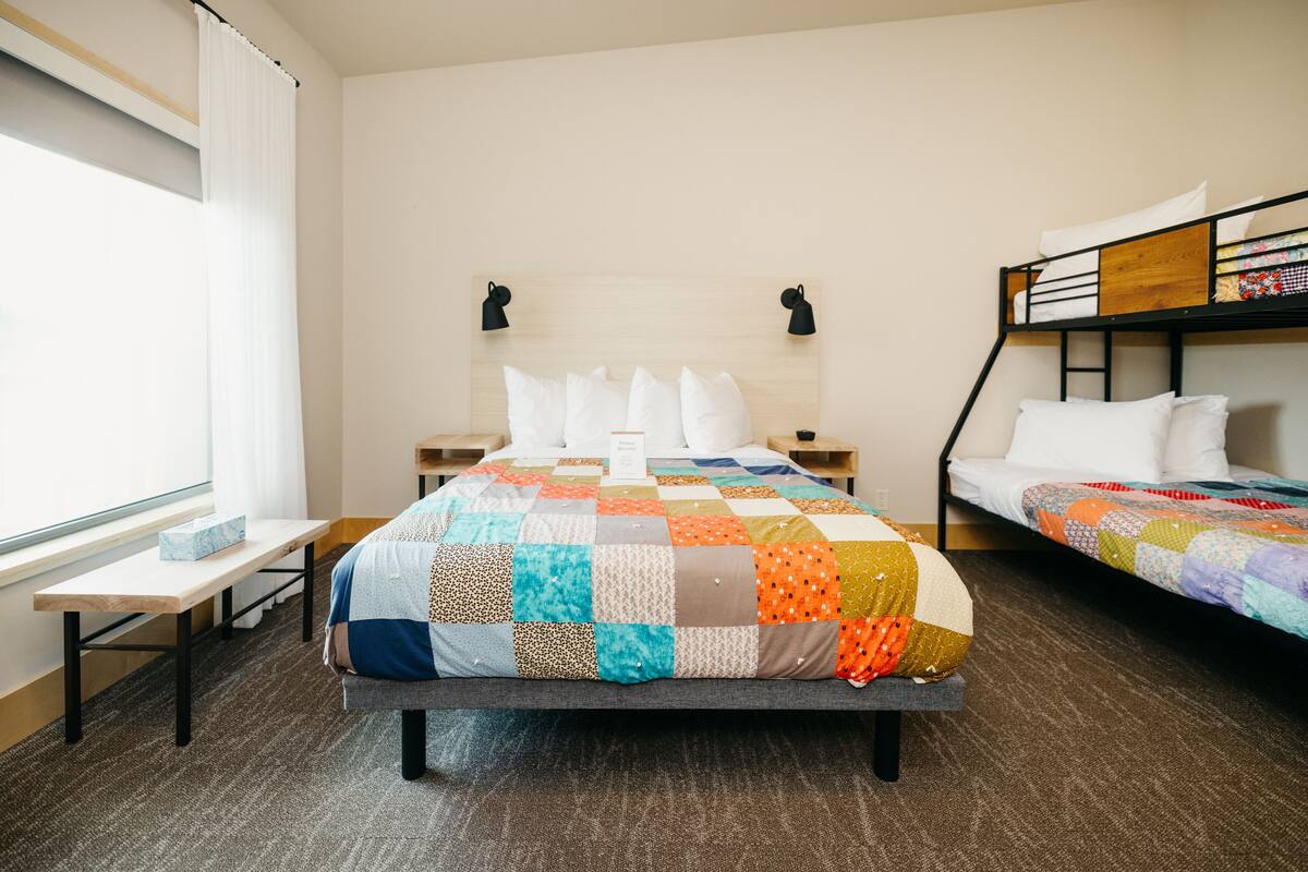 Een kamer met een groot bed, een kleiner bed, een bureau en een raam.