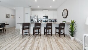Une cuisine moderne avec des meubles blancs, un îlot central doté de tabourets et une horloge au mur.