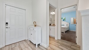 Un couloir avec une porte blanche, une console blanche et une chambre à coucher visible à travers une porte ouverte.