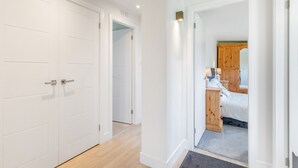 Un pasillo con puertas blancas, piso de madera y una cama con cabecera de madera en la habitación contigua.