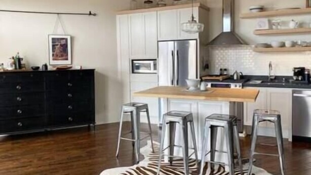 A modern kitchen with white cabinets, a wooden countertop, stainless steel appliances, and bar stools. - The Quarters | Suite 5 (Grafton)