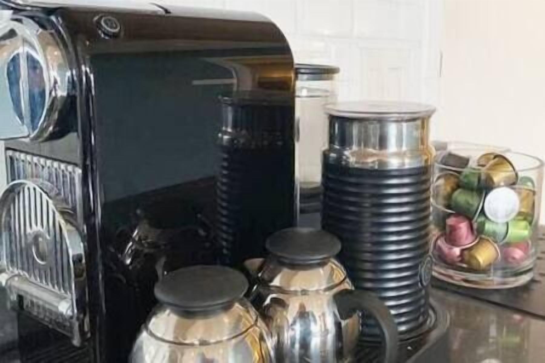A kitchen with a coffee maker, stainless steel pots, and a container with colorful items.