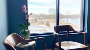 A room with a large window, two wooden chairs, and a potted plant. - The Quarters | Suite 5 (Grafton)