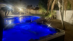 Een hottub met blauwe verlichting, omgeven door palmbomen en een overdekt terras.