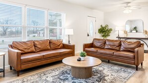 A living room with two brown leather sofas, a round coffee table, and a patterned rug. - Renovated 5BR | Group Space + Large Yard (Wentzville)