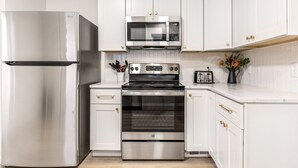 A modern kitchen with white cabinetry, stainless steel appliances including a refrigerator, microwave, and oven, and a countertop with a coffee maker and utensils. - Renovated 5BR | Group Space + Large Yard (Wentzville)