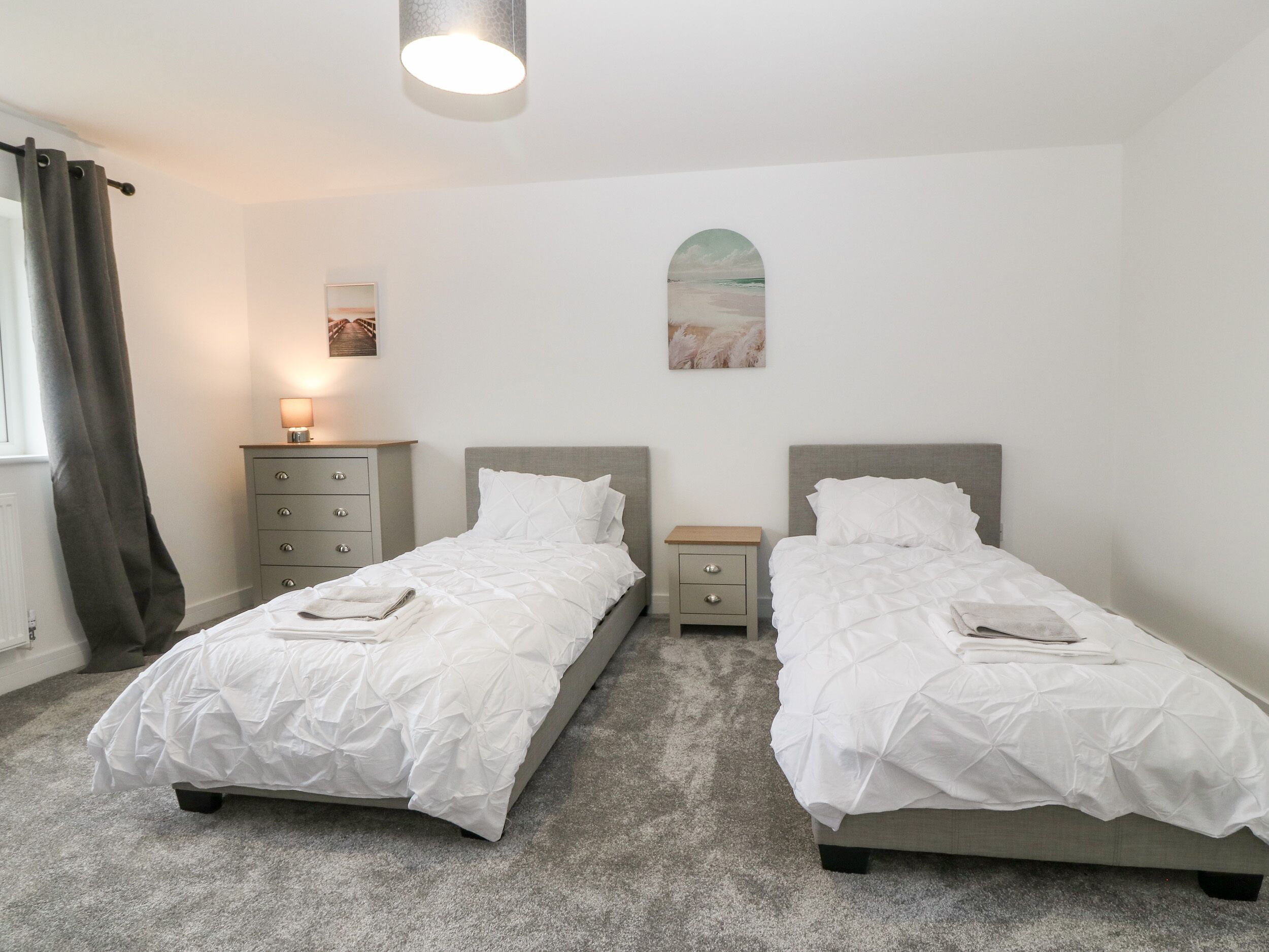 Une chambre avec deux lits simples, une table de chevet, une lampe et un tableau au mur.