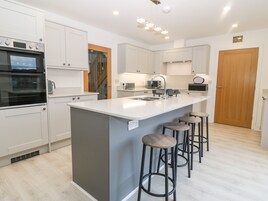 A modern kitchen with white cabinets, a central island with stools, a built-in oven, and a wooden door.