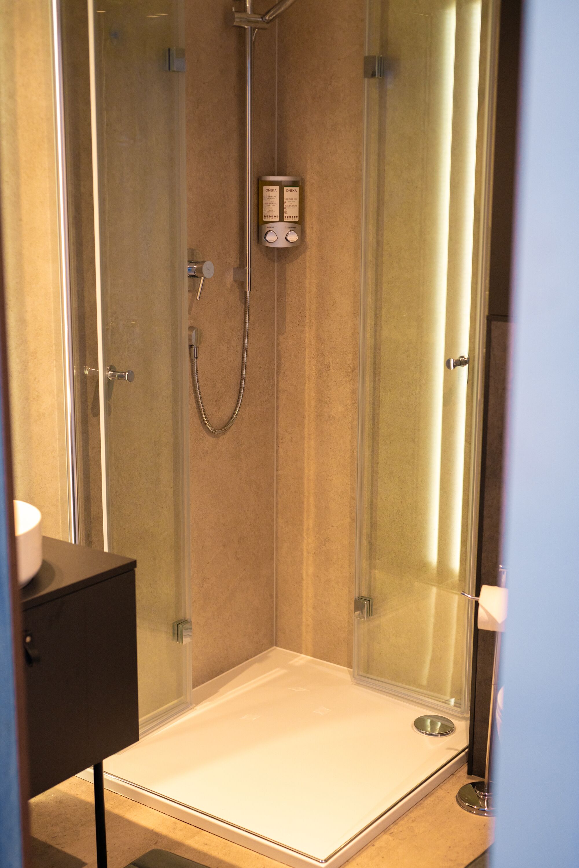 Une cabine de douche moderne dotée d’une porte en verre, d’un panneau de commande et d’un sol blanc.