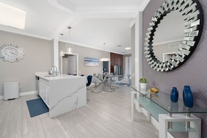 Cozinha moderna com ilha de mármore, sala de jantar com mesa de vidro e um espelho decorativo grande.
