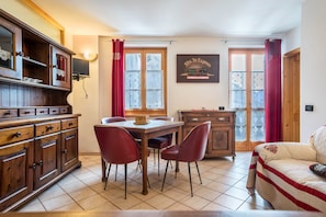 A room with a wooden dining table, red chairs, a sofa, a wooden cabinet, and a television mounted on the wall. - Apartment 'Appartamento Cocodi' with Mountain View, Shared Garden and Balcony (Caldes)