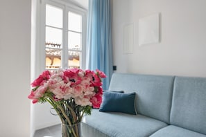 Une pièce avec un canapé bleu clair, un vase contenant des fleurs roses et blanches, et une fenêtre ornée de rideaux bleus.