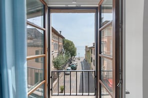 Une vue à travers une fenêtre donnant sur un balcon, une rue bordée de voitures garées et des bâtiments en arrière-plan.