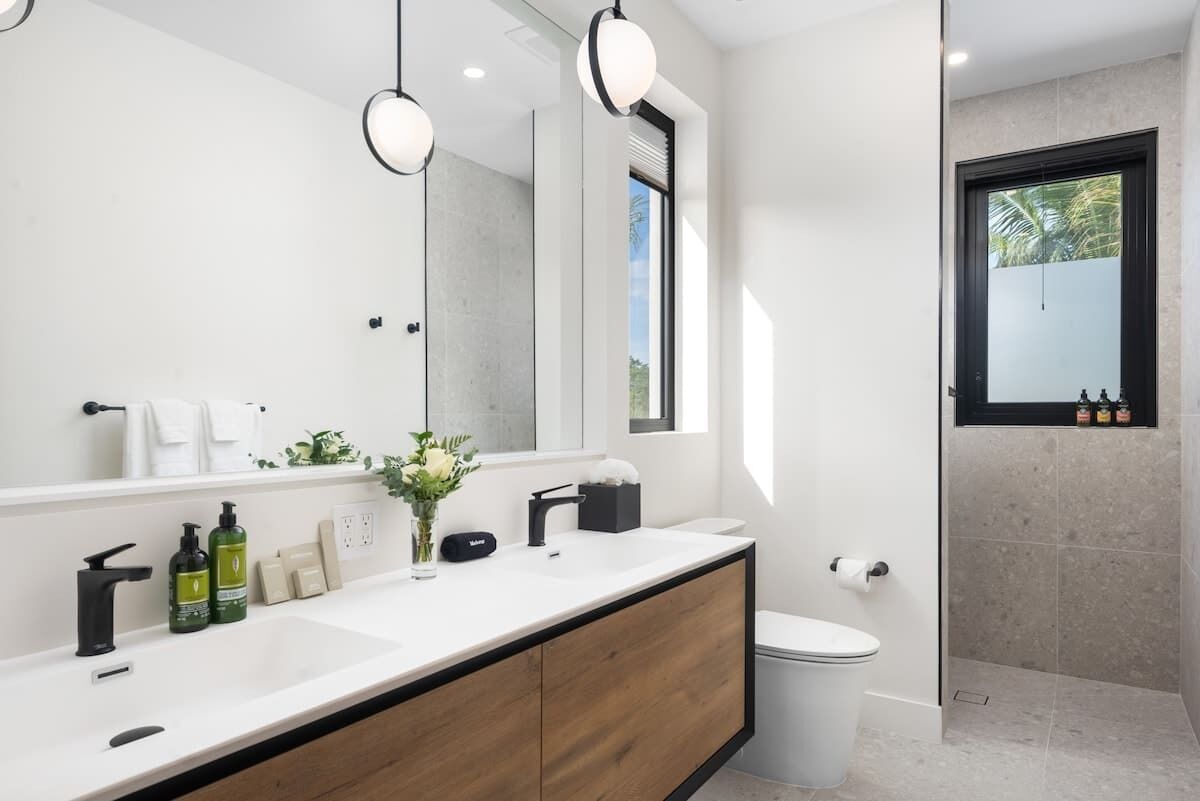 Ein modernes Badezimmer mit großem Spiegel, Holzschrank, Toilette und Duschbereich.