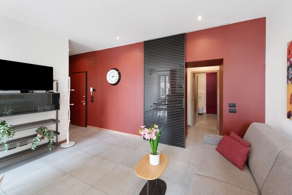 A modern living room with a flat-screen TV, a clock, a potted plant, and a sofa.