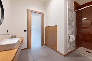 Une salle de bain moderne avec un grand lavabo, une douche dotée d’une porte en verre et une porte en bois.