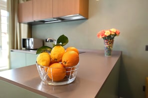 Uma bancada de cozinha com uma tigela de vidro cheia de laranjas e um vaso de flores.