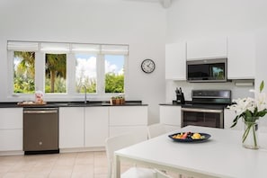 A modern kitchen with white cabinets, a dishwasher, a microwave, and a dining table with a plate of fruit.