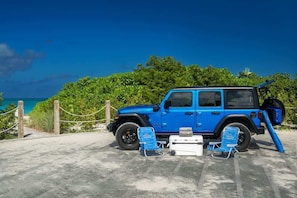 A blue off-road vehicle parked on a concrete surface with beach views and greenery in the background.