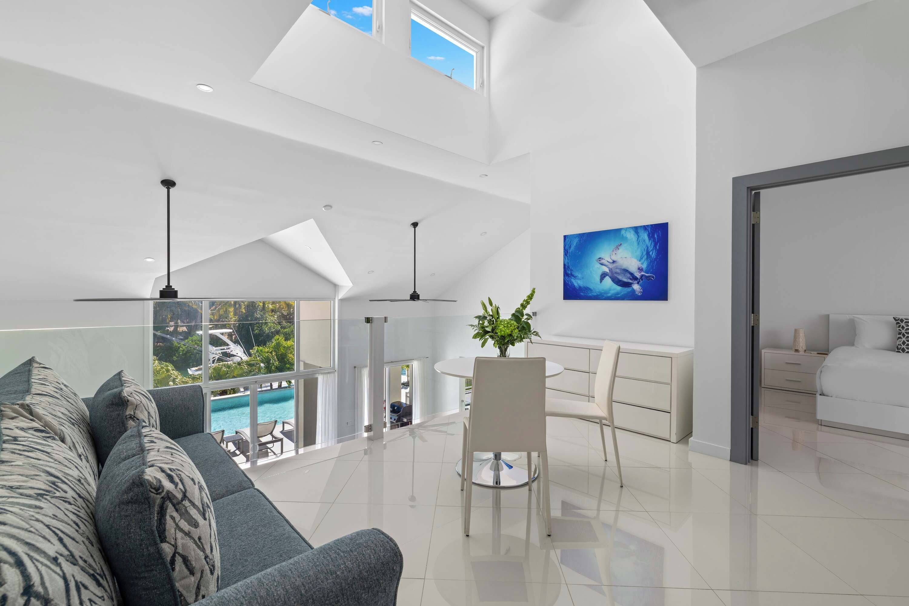 Una sala de estar moderna con vista a una piscina y un área exterior, un comedor con mesa y sillas blancas, y un dormitorio con cama y mesita de noche.