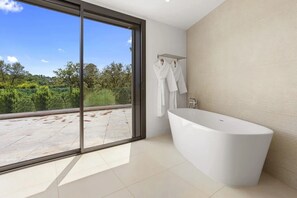 A modern bathroom with a freestanding bathtub, a glass door leading to an outdoor area, and a towel rack with white towels. - Apartment 'Grand Appartement Valeriane' with Mountain View, Shared Pool and Wi-Fi (Trans-en-Provence)